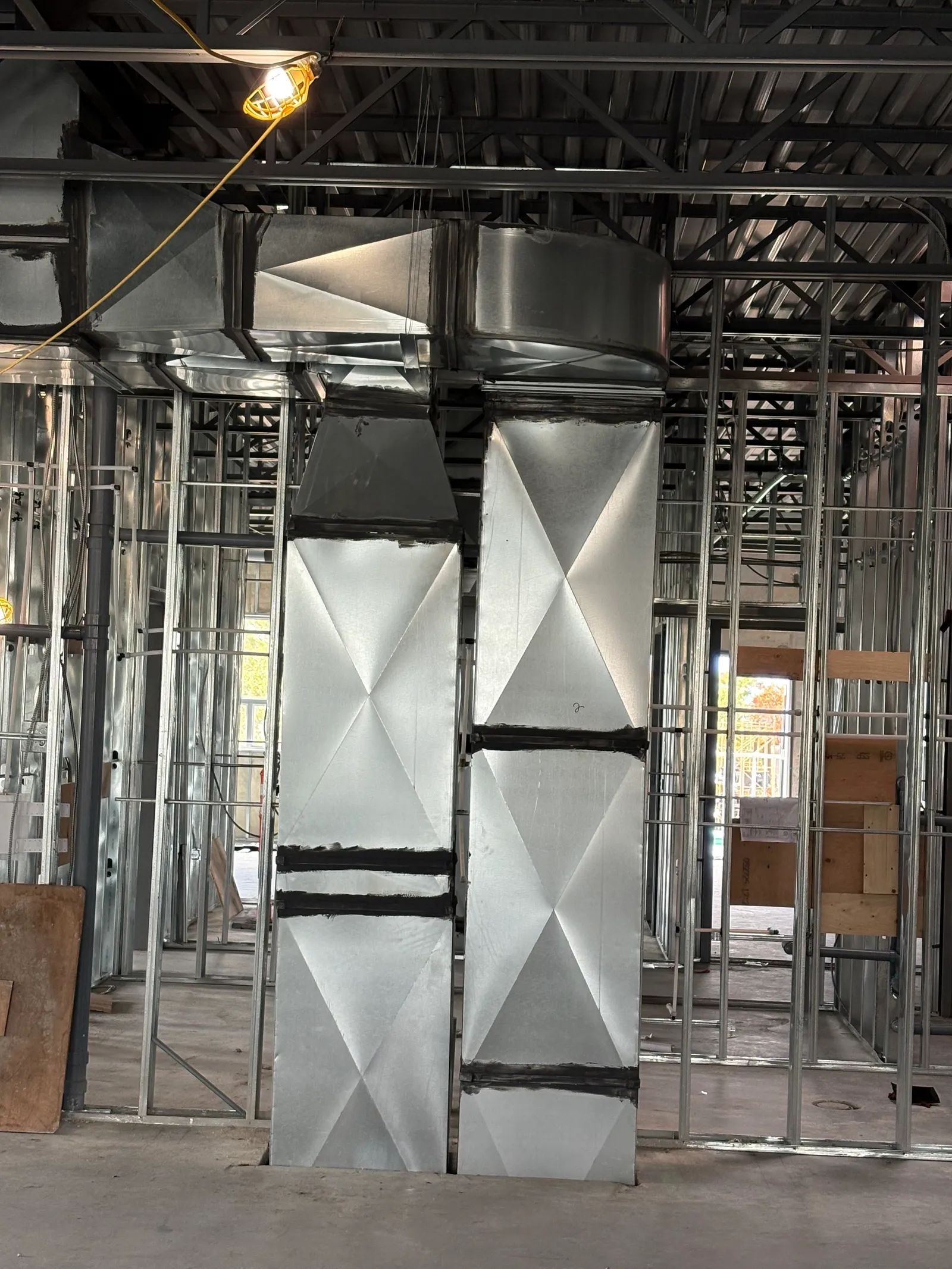 Custom-fabricated rectangular sheet metal duct risers with sealed seams in a steel-stud build