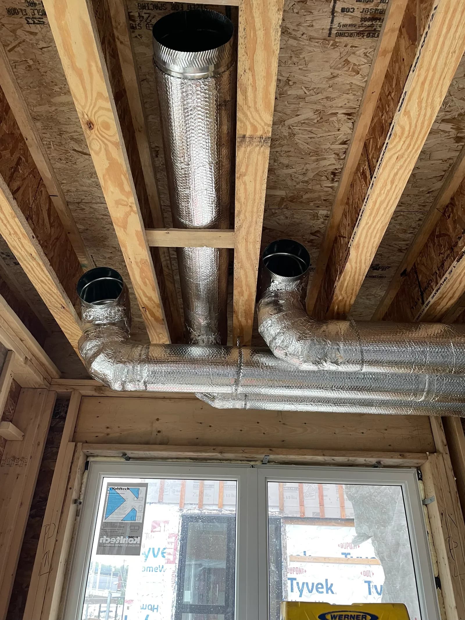 Insulated flexible ductwork and sheet metal collars run through a wood-framed home ceiling